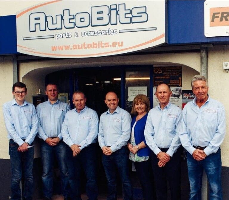 Team of staff members standing outside the AutoBits car parts and accessories shop beneath the AutoBits storefront sign.